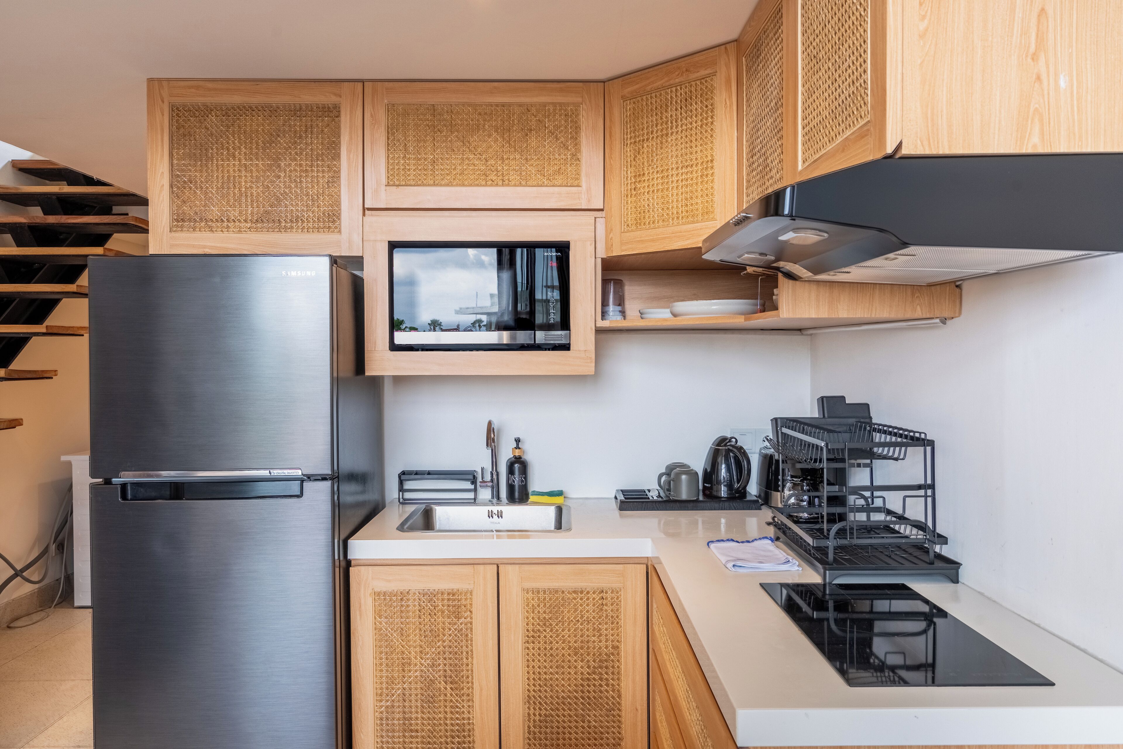 A modern kitchen with wooden cabinets, a stainless steel refrigerator, a microwave, and a black stove.