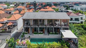 A modern two-story building with a swimming pool, surrounded by residential houses with red roofs.