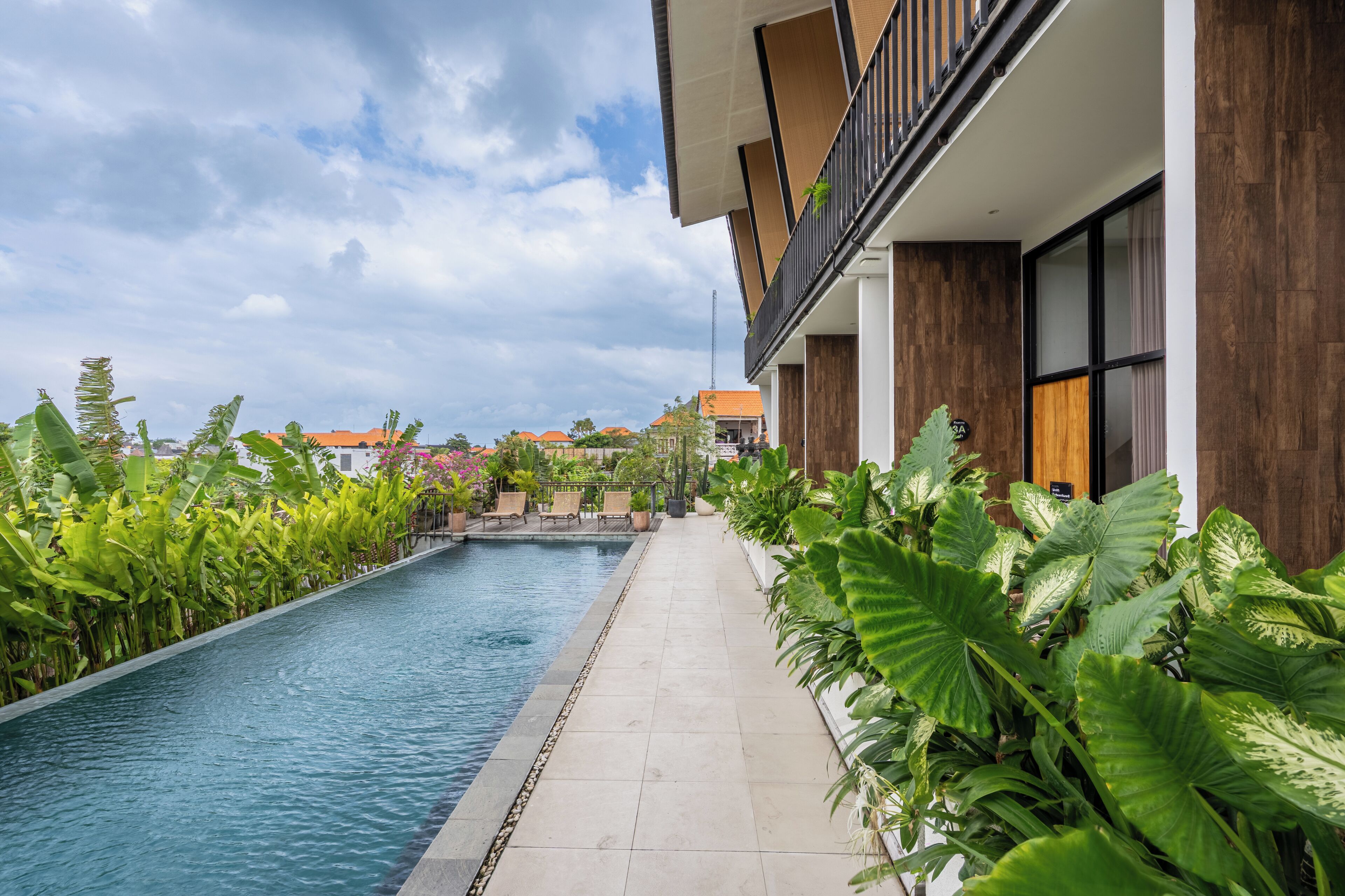 Un hotel moderno con piscina, abundante vegetación y vistas a otros edificios.