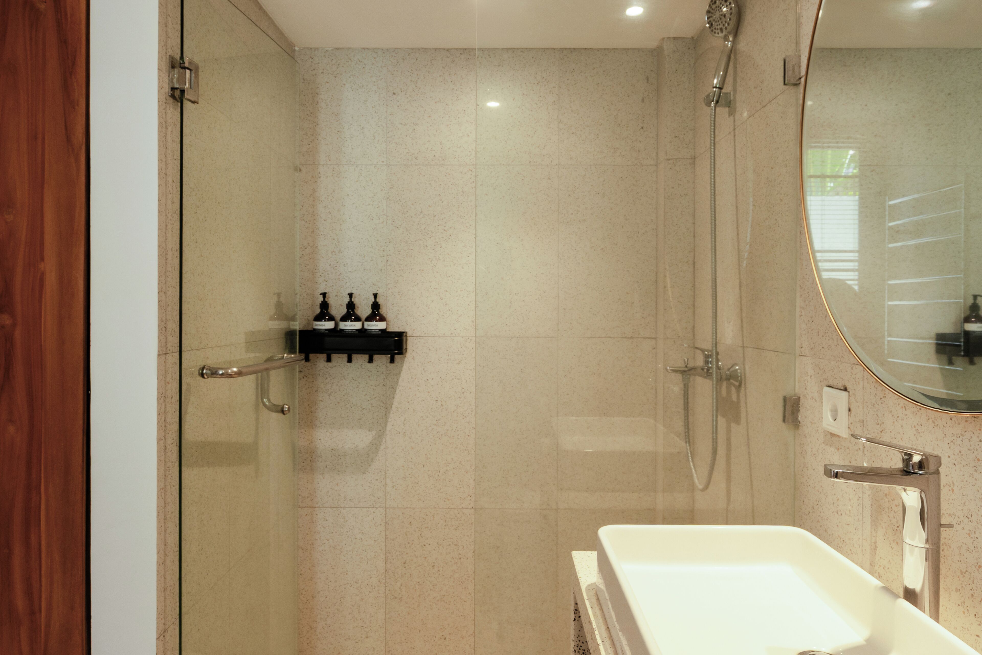 A modern bathroom with a glass shower enclosure, a white sink, and a mirror.