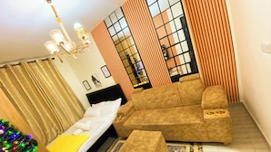 Habitación de hotel con cama, sofá, pequeño otoman, árbol de Navidad y ventana con persianas.