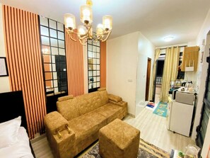 Une chambre d’hôtel équipée d’un canapé, d’un pouf et d’un coin repas avec un réfrigérateur.