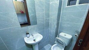 Une petite salle de bain avec un lavabo, des toilettes et un seau vert.