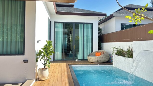 A modern outdoor pool area with a wooden deck, a lounge chair, and a glass door leading to a covered patio. - Narinsaya Pool villas (Sa Khu)