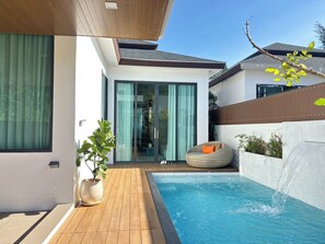 Ein moderner Poolbereich im Freien mit Holzterrasse, Liegestuhl und einer Glastür zu einer überdachten Terrasse.