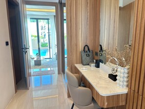 Ein modernes Badezimmer mit Marmorplatte, Waschbecken und Spiegel. Eine Holzverkleidung und Blick auf einen Außenpoolbereich sind ebenfalls vorhanden.