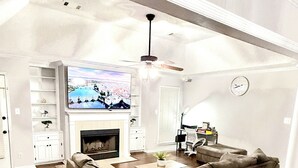 Ein geräumiges Wohnzimmer mit einem großzügigen, L-förmigen Ecksofa, einem Kamin, einem Fernseher und einem Deckenventilator.