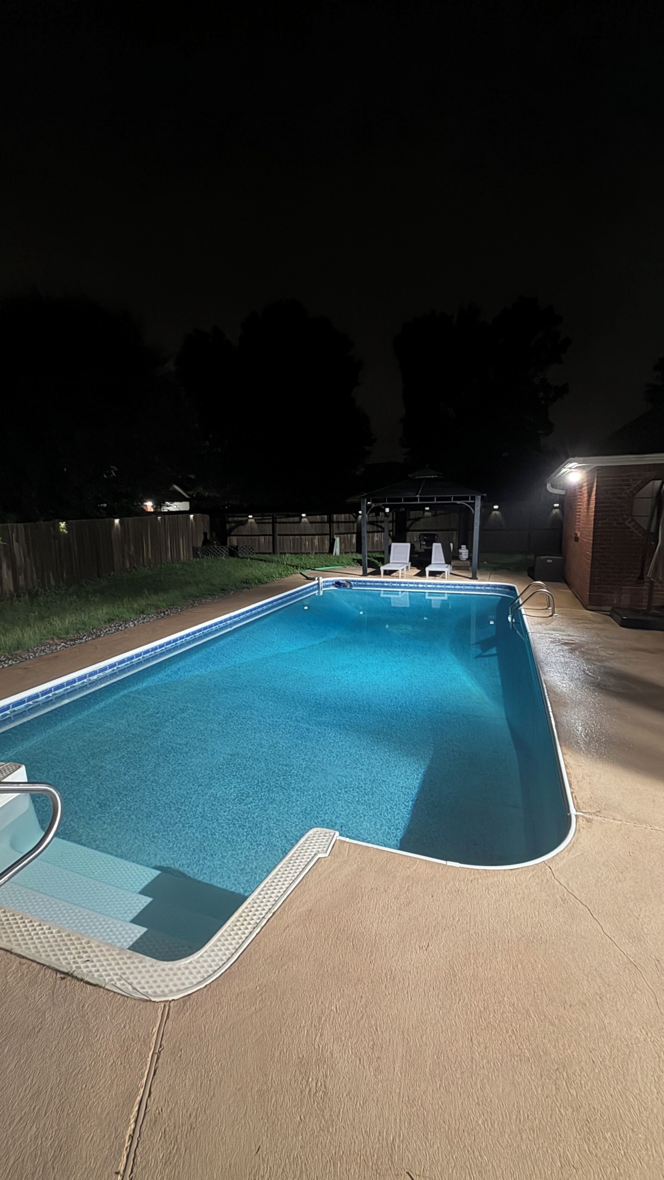 A swimming pool with a built-in hot tub, surrounded by a wooden fence and a brick wall.