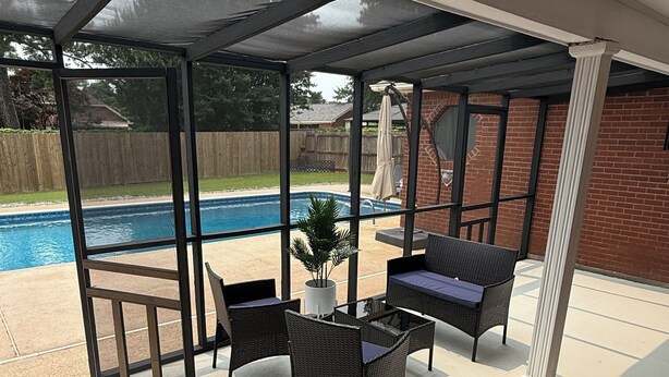 Eine überdachte Terrasse mit Gartenmöbeln, einem Pool und Blick auf einen Garten.
