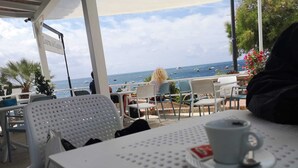 Une terrasse dotée de chaises et de tables blanches, offrant une vue sur la mer et les bateaux.
