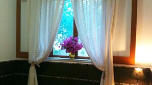 Une chambre à coucher avec un lit, une fenêtre avec des rideaux, un vase de fleurs et une table de chevet avec une lampe.