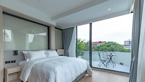 Une chambre moderne avec un grand lit, une table de chevet, une petite table avec des chaises et un balcon offrant une vue sur la ville.