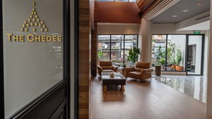 Un hall d’hôtel moderne avec un mur de verre sur lequel est affiché le nom de l’hôtel, des fauteuils en cuir, une table basse et de grandes fenêtres offrant une vue sur la ville.