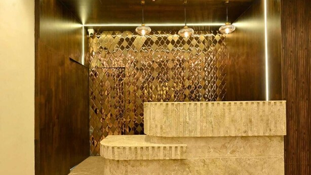 A modern bathroom with a marble sink, a decorative wall with a diamond pattern, and three pendant lights. - Vastu Inn (Rourkela)