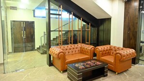 A modern living room with a glass wall, a staircase, and a brown leather sofa set. - Vastu Inn (Rourkela)
