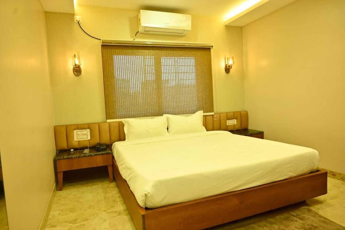 Habitación de hotel con una cama grande, mesitas de noche, una ventana con persianas y un equipo de aire acondicionado.