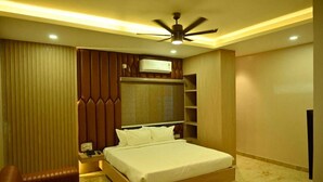 A bedroom with a bed, a nightstand, a desk, a chair, a ceiling fan, and built-in shelving. - Vastu Inn (Rourkela)