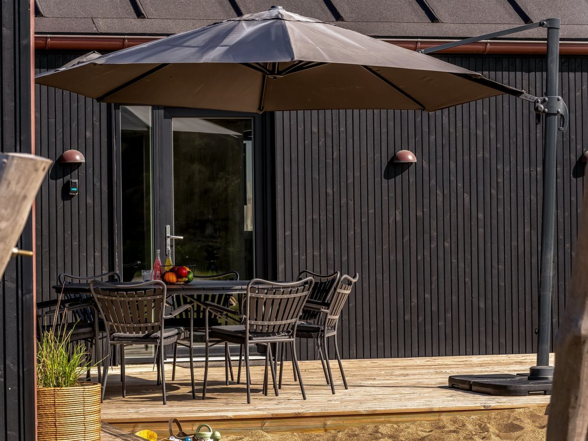 An outdoor dining area with a table and chairs, a large umbrella, and a wooden deck.