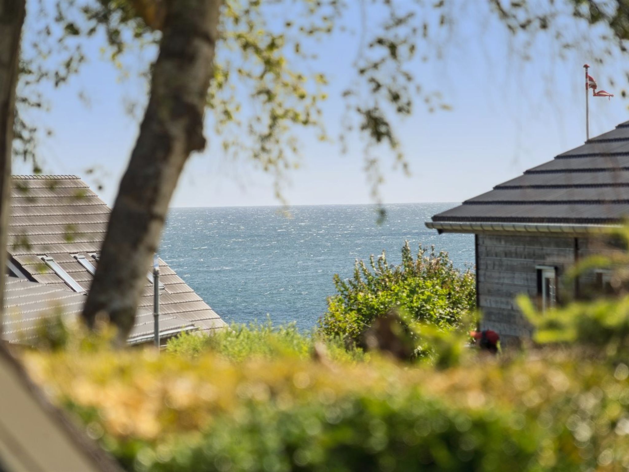 A coastal building with a view of the sea, a flag on top, and a tree in the foreground.