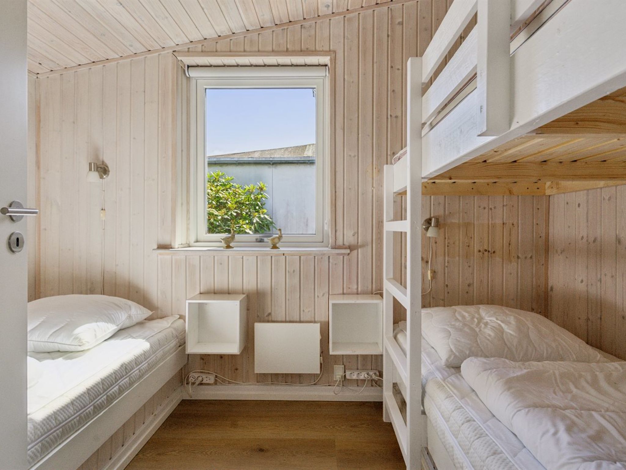 Una habitación compacta con literas, un ventanal con vistas a zonas verdes y una pared de madera.