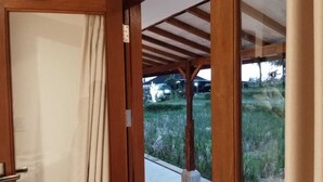 A wooden-framed door leading to a covered outdoor area with a bench and a view of a grassy landscape. - Rumah Kemuning Bali (Bali)