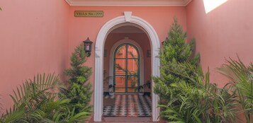 A villa entrance with a checkered floor, an archway, and potted plants.