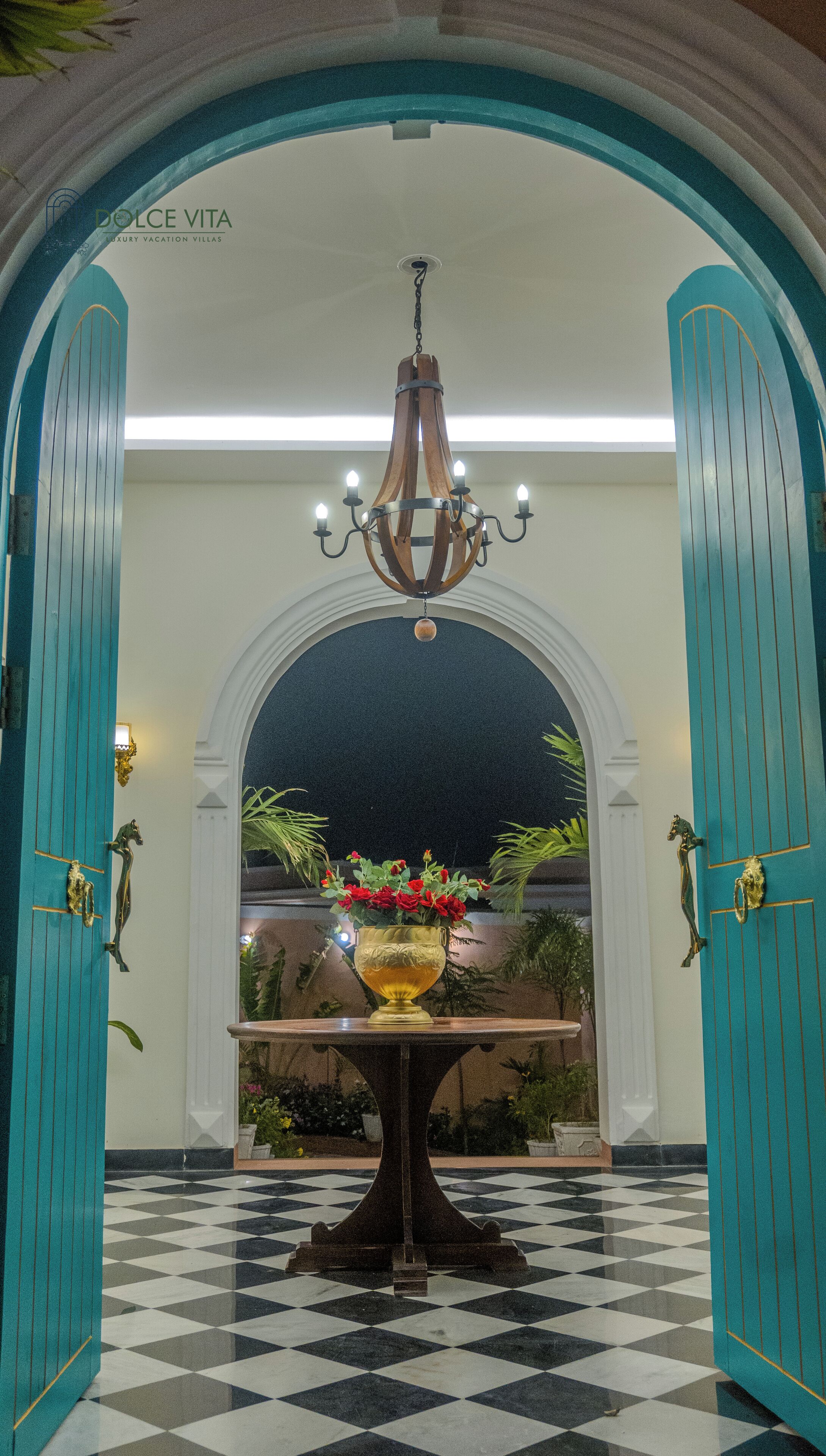 A lobby with a chandelier, a table with a vase of flowers, and a checkered floor.