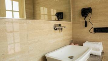 A bathroom with a large bathtub, a mirror, a hairdryer, and toiletries on the counter.