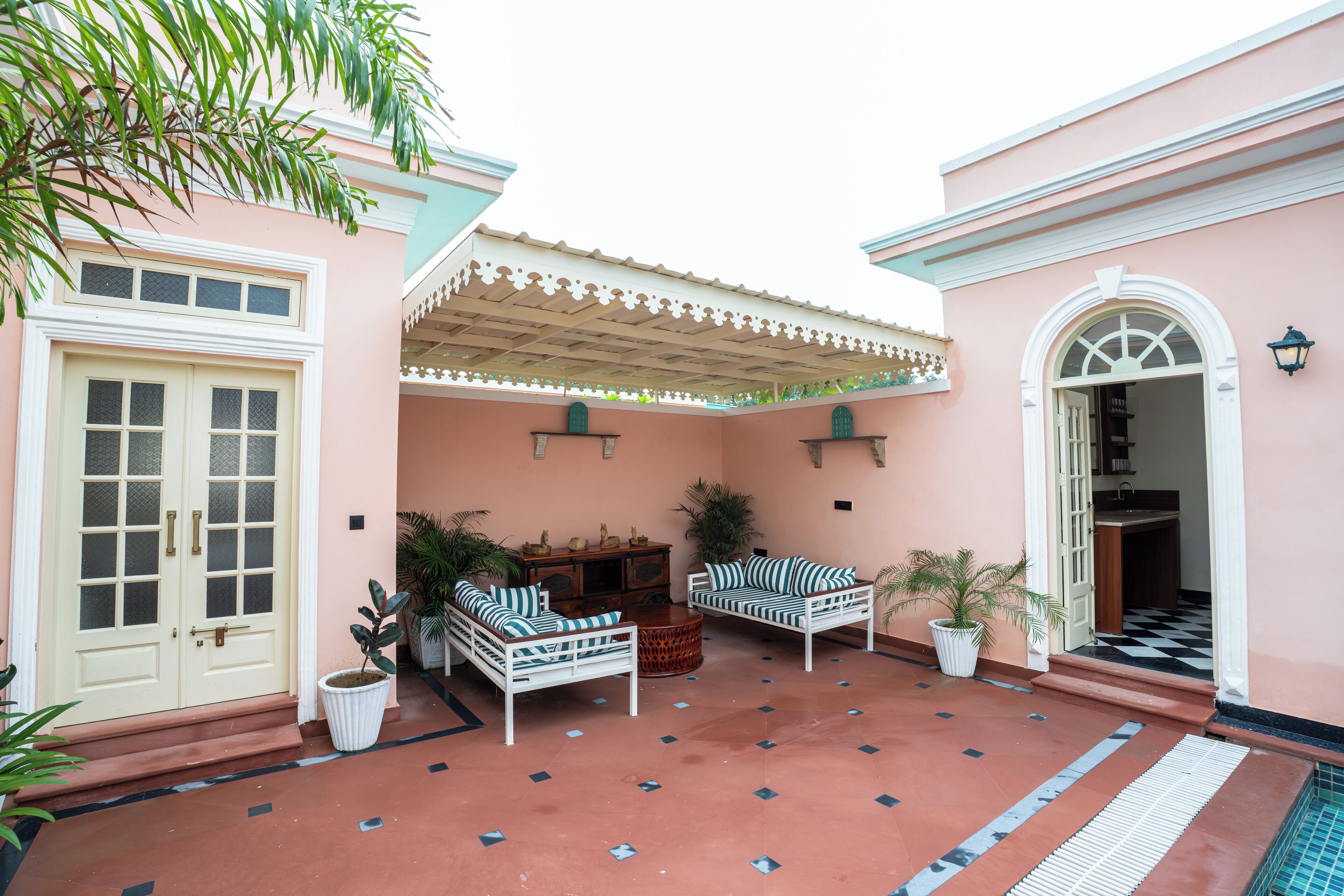 A pink building with a covered patio, two white sofas, a wooden cabinet, and potted plants.