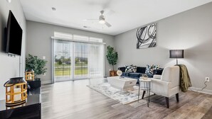 A spacious living room with a large sliding glass door leading to a balcony, a flat-screen TV mounted on the wall, a dark blue sofa with decorative pillows, and a modern coffee table. - Work + Relax | Luxury Escape (Whitestown)