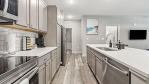 A modern kitchen with stainless steel appliances, a large island with a sink, and a flat-screen TV mounted on the wall. - Work + Relax | Luxury Escape (Whitestown)
