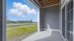A covered porch with a concrete floor and a view of a grassy area and buildings in the background. - Work + Relax | Luxury Escape (Whitestown)