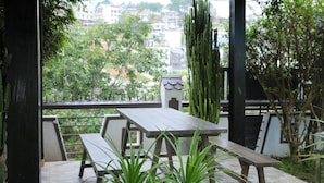 A covered patio with a wooden table and benches, surrounded by potted plants and a view of buildings and trees. - 7 bedroom villa Flamingo Danang (Da Nang)