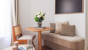 Une petite pièce accueillante, avec une table en bois, une chaise, un canapé avec des coussins, un tableau noir fixé au mur et un vase de fleurs posé sur la table.