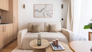 Un salon moderne avec un canapé, deux coussins, une table basse ornée d’un vase et de bougies, et un tableau abstrait encadré accroché au mur.