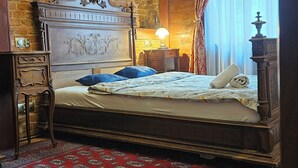 Een slaapkamer met een bakstenen muur, een groot bed met een houten hoofdeinde, een rood tapijt met patroon en een kroonluchter.