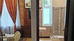 Een kamer met een bed, een vloerkleed, een houten vloer, een badkamer met douche, en een deur naar buiten.