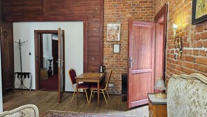 Een knus vertrek met een houten tafel en stoelen, een rode deur en een bakstenen muur.