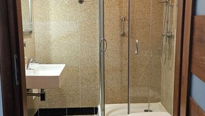 Een badkamer met een douche met glazen wand, een witte wastafel en een toilet.