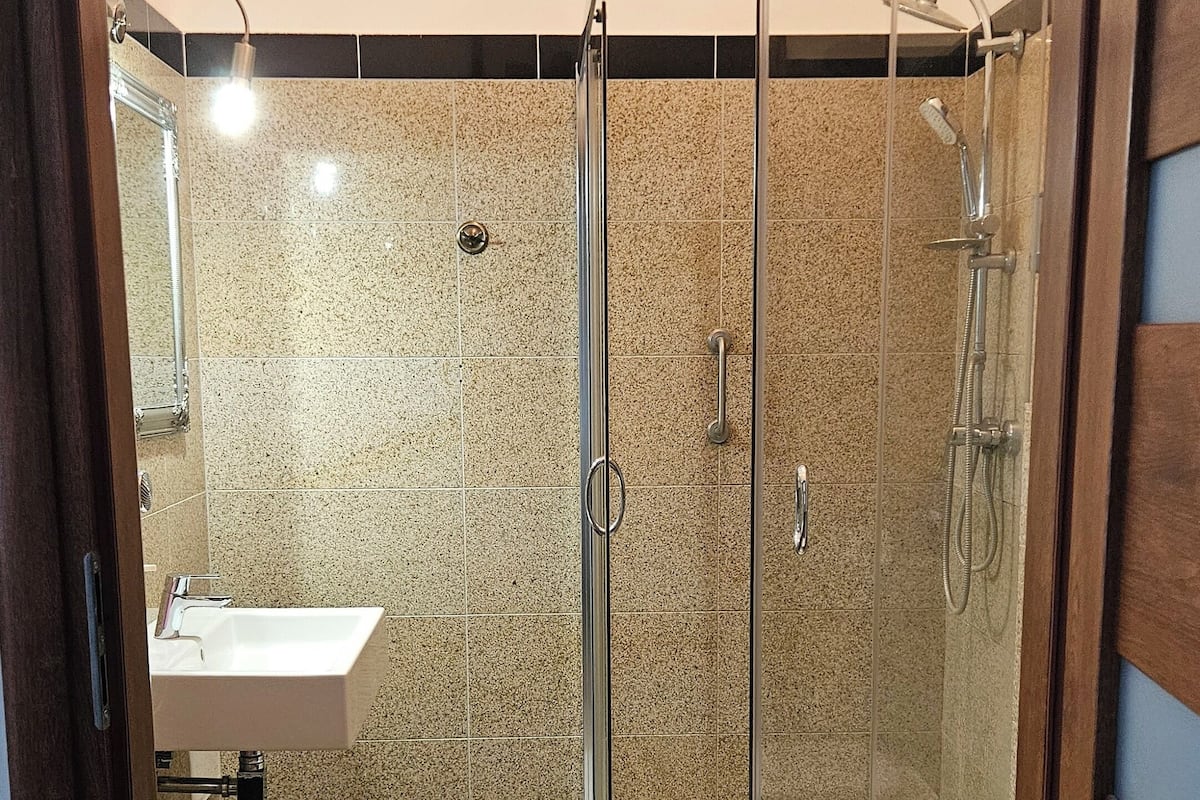 Un baño con ducha envuelta en vidrio, un lavabo blanco y un inodoro.