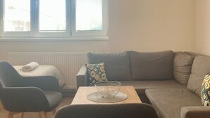 A modern living room with a grey sofa, a black chair, and a small table with a wire basket. - Spacious 2-bedroom apartment in Lučenec (Banskobystrický kraj)