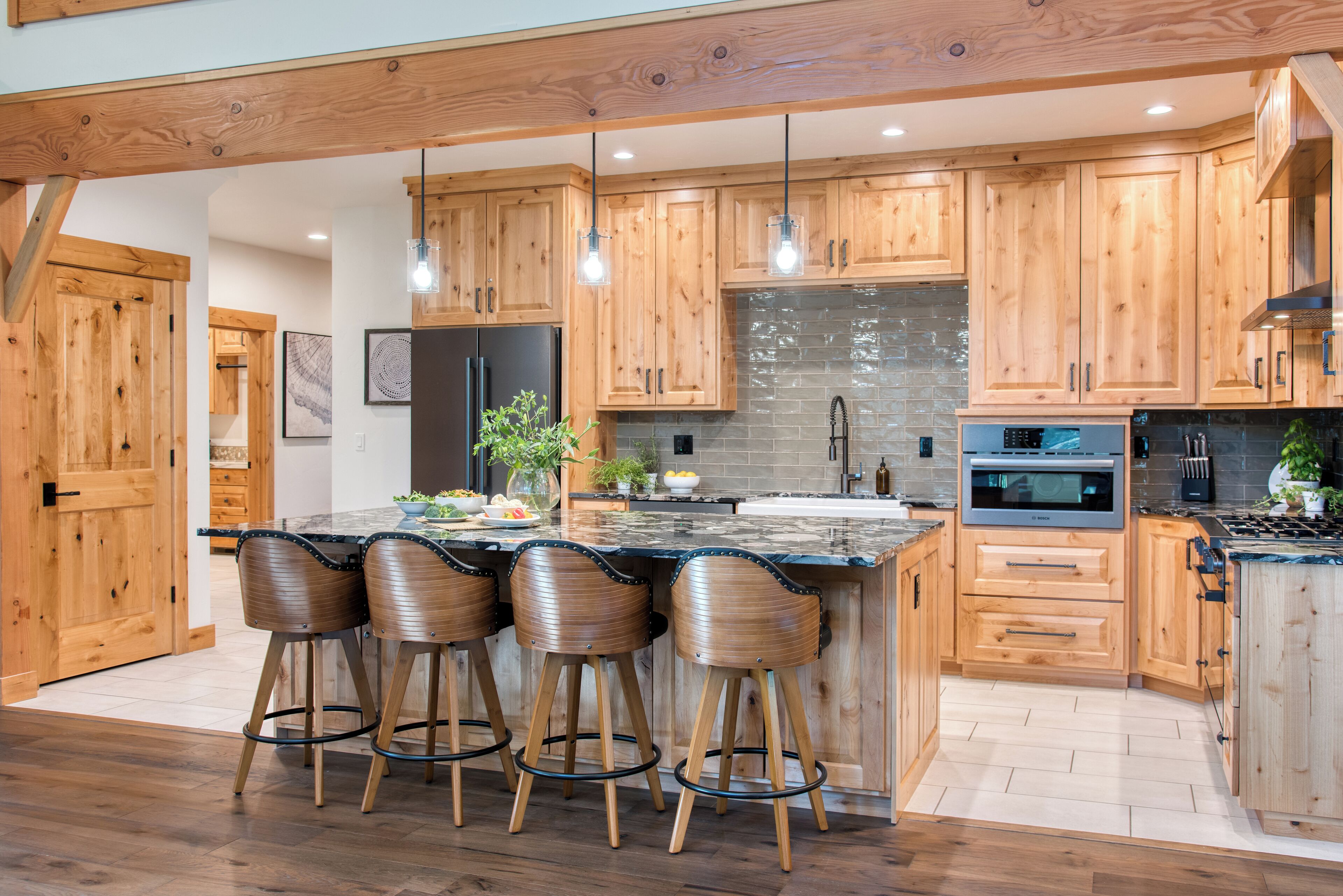 A modern kitchen with wooden cabinets, a large island with bar stools, a stone backsplash, and stainless steel appliances.