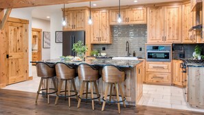 Una cocina moderna con armarios de madera, una isla grande con taburetes de bar, salpicadero de piedra y electrodomésticos de acero inoxidable.