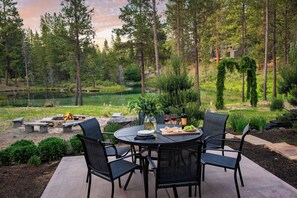 An outdoor dining area with a round table, four chairs, and a view of a pond surrounded by trees.