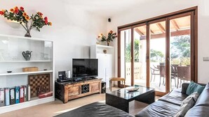 A modern living room with a sofa, coffee table, TV, bookshelf, and a sliding glass door leading to an outdoor patio.