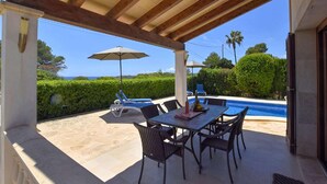 An outdoor patio with a pool, covered seating, and a table with chairs.