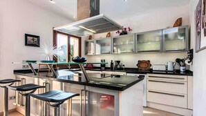 A modern kitchen with a central island, bar stools, stainless steel appliances, and a large window providing natural light.