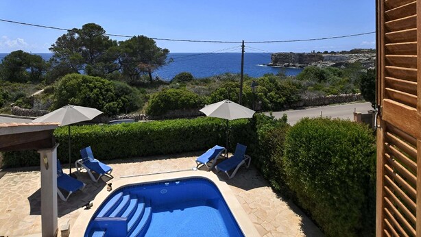 A swimming pool with lounge chairs and umbrellas, overlooking a coastal landscape with trees and a view of the sea.