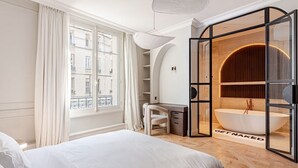 Una habitación de hotel moderna con una cama grande, un escritorio y una bañera independiente.
