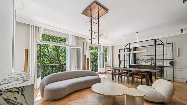 Un salón amplio con un gran ventanal, un sofá moderno, una zona de comedor y una lámpara de techo original.